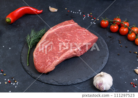 Raw fresh marbled meat and seasonings on dark background Raw fresh marbled meat and seasonings on dark background 111297523