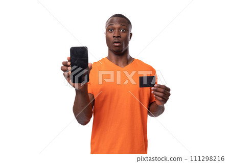 young surprised african man dressed in orange t-shirt holding phone and credit card. advertising 111298216