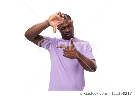 young cheerful african man with a short haircut dressed in a lilac t-shirt makes a grimace 111298217