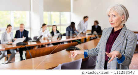 Portrait of an elderly successful businesswoman in meeting room against the backdrop of team of her colleagues 111298543