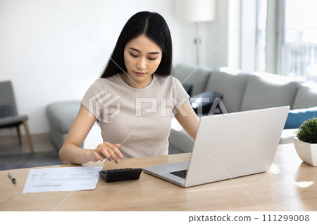 Focused young Asian homeowner woman calculating domestic expenses Focused young Asian homeowner woman calculating domestic expenses 111299008
