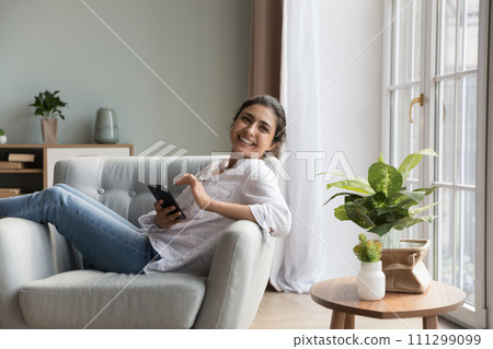 Pretty Indian woman relaxing on armchair smile use cell phone Pretty Indian woman relaxing on armchair smile use cell phone 111299099