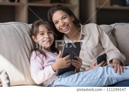 Woman and daughter resting on sofa with digital tablet device Woman and daughter resting on sofa with digital tablet device 111299147
