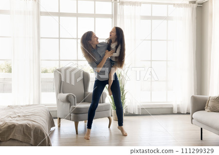 Young mother standing indoors holding little daughter in her arms 111299329