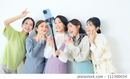 Casual group of women taking selfies with selfie sticks 111300034