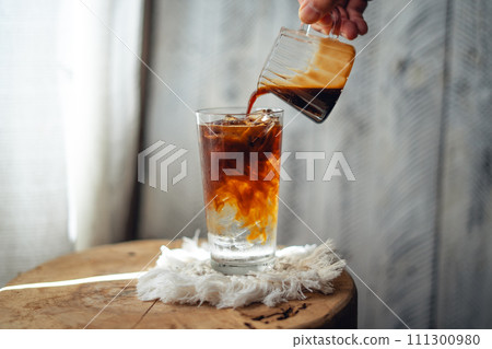 Iced coffee,Pouring a shot of coffee into cold water in a glass Iced coffee,Pouring a shot of coffee into cold water in a glass 111300980