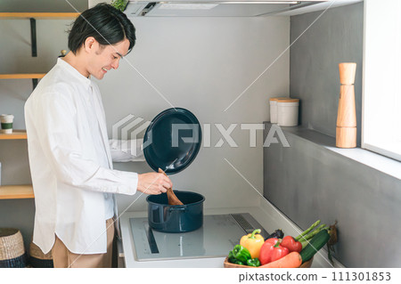 A young man (homemaker/househusband) cooking stew on a HI stove in the kitchen 111301853