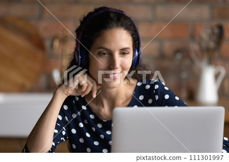 Close up smiling woman in headphones looking at laptop screen 111301997
