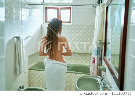 Back view of woman towel drying hair in vintage bathroom, post-bath routine in tiled interior, hygiene concept. Natural light through window, fresh clean cozy setting with sink, shower curtain. Back view of woman towel drying hair in vintage bathroom, post-bath routine in tiled interior, hygiene concept. Natural light through window, fresh clean cozy setting with sink, shower curtain. 111303755