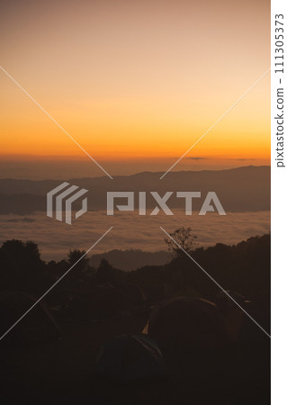 travel and people activity concept with large pine and camping tent with layer of mountain and cloudy sky background 111305373