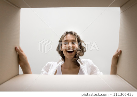 Excited happy young woman looking inside cardboard box with surprise 111305433