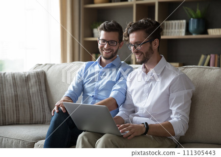 Two adult brothers relax at home use laptop 111305443
