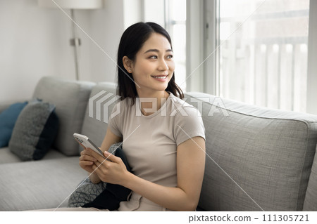 Happy relaxed young Asian woman using cellphone at home 111305721