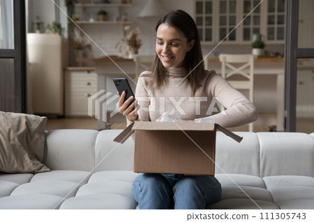 Woman sit on sofa with parcel and smartphone 111305743
