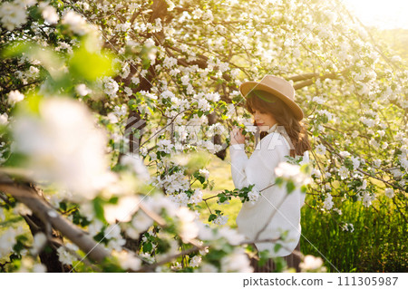 Smiling woman with hat posing in blooming spring park. The concept of relax, travel. Fashion style. 111305987