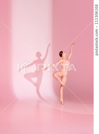 Pastel Pirouette. Young woman, ballerina dancer in pink ensemble poses against soft background. Her shadow dances in tandem. Pastel Pirouette. Young woman, ballerina dancer in pink ensemble poses against soft background. Her shadow dances in tandem. 111306108