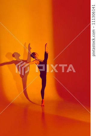 Flexibility in Neon Glow. Beautiful woman stretches gracefully in black sports overalls, barefoot in neon-lit studio, shadow mirroring her movements. Flexibility in Neon Glow. Beautiful woman stretches gracefully in black sports overalls, barefoot in neon-lit studio, shadow mirroring her movements. 111306141