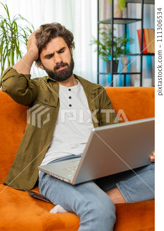 Middle eastern young man use laptop surprised by bad news, fortune loss fail lottery results at home 111306534