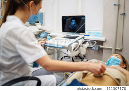 Doctor makes patient women abdominal ultrasound. Ultrasound Scanner in hands of doctor. Diagnostics. Doctor makes patient women abdominal ultrasound. Ultrasound Scanner in hands of doctor. Diagnostics. 111307178