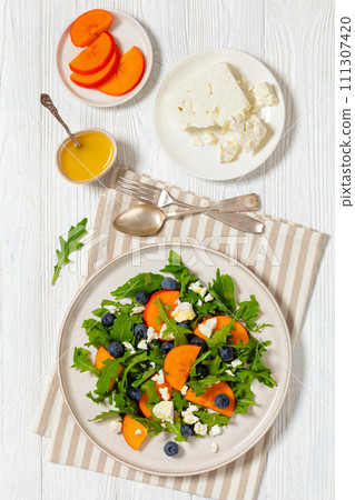 arugula persimmon cheese berries salad, top view arugula persimmon cheese berries salad, top view 111307420
