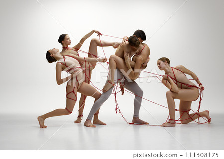 Jealousy and passion. Ballet dancers connected with red ribbons against white studio background. Love, affection and manipulation of society 111308175
