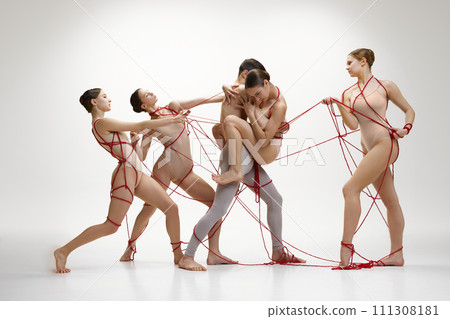 Ballet dancers in beige costumes, connected with red ribbons performing against white studio background. Inner fears, support, help and manipulation Ballet dancers in beige costumes, connected with red ribbons performing against white studio background. Inner fears, support, help and manipulation 111308181