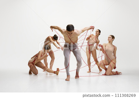Leaving comfort zone, freedom. Male ballet dancer connected with red strings to ballerinas against white studio background Leaving comfort zone, freedom. Male ballet dancer connected with red strings to ballerinas against white studio background 111308269