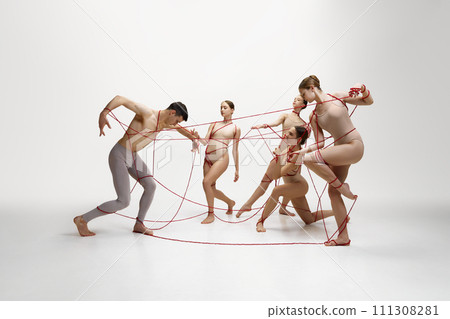 Graceful ballet dancers performing with red string connected to young man against white studio background. Social connections 111308281