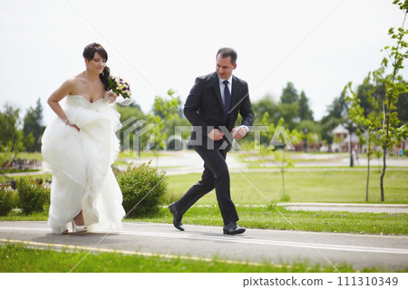 The bride and groom run along the road together 111310349