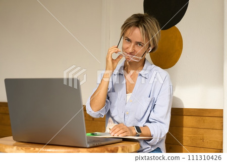 Woman sitting at cafe table and working on laptop computer. Female surfing internet on laptop using 111310426