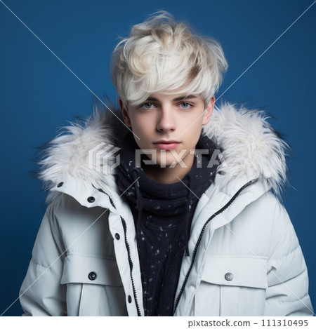 Teenage boy in a white winter coat. Studio portrait of a teenager in a winter jacket smiling on a blue background looking at the camera. Happy european young adult wearing warm winter clothes. 111310495