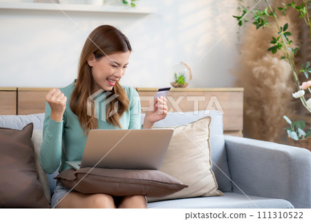 Young asian woman sitting on sofa using laptop computer shopping online with credit card buying. 111310522