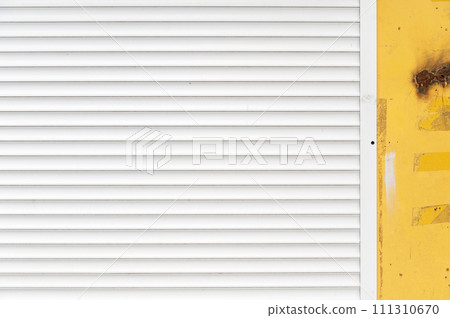 White blinds on the yellow wall of the garage. Yellow textured concrete wall with white blinds background. White blinds on the yellow wall of the garage. Yellow textured concrete wall with white blinds background. 111310670