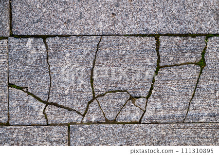 Old grey granite tiles are laid on the streets of the city. Cracked granite tiles 111310895