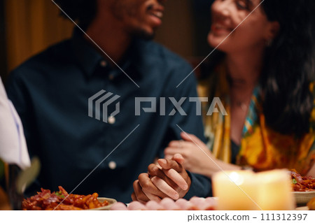 Hands of two young intercultural sweethearts looking at one another while sitting by served table in front of camera and having dinner 111312397