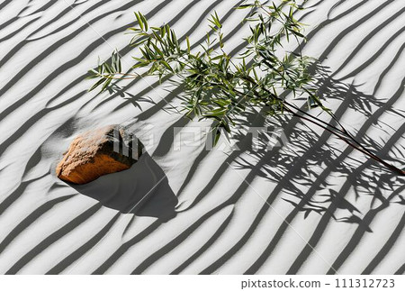 Bamboo leaves and rocks on white sand dune with shadow. 111312723
