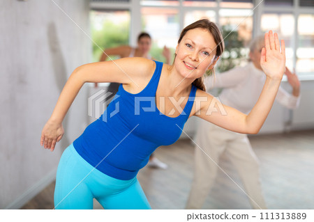 Smiling woman practicing rhythmic aerobics during group workout Smiling woman practicing rhythmic aerobics during group workout 111313889