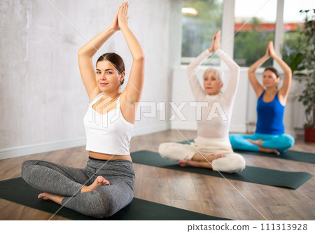 Active women practice pose sitting cross-legged with their arms raised 111313928