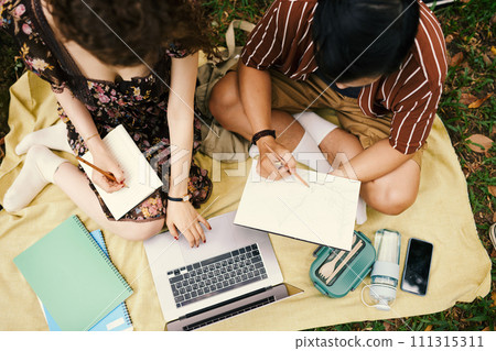 Above view of two young students from faculty of design sitting in front of laptop and drawing sketches in copybooks or notepads Above view of two young students from faculty of design sitting in front of laptop and drawing sketches in copybooks or notepads 111315311