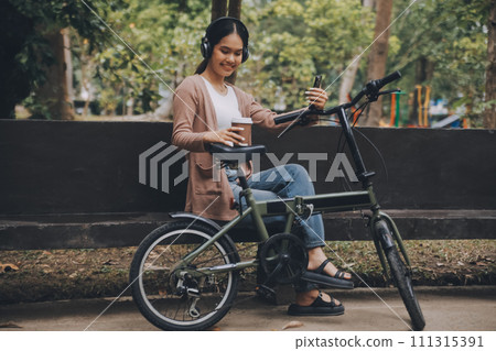Happy young Asian woman while riding a bicycle in a city park. She smiled using the bicycle of transportation. Environmentally friendly concept. 111315391