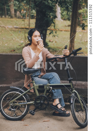 Happy young Asian woman while riding a bicycle in a city park. She smiled using the bicycle of transportation. Environmentally friendly concept. 111315392