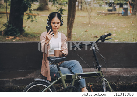 Happy young Asian woman while riding a bicycle in a city park. She smiled using the bicycle of transportation. Environmentally friendly concept. 111315396