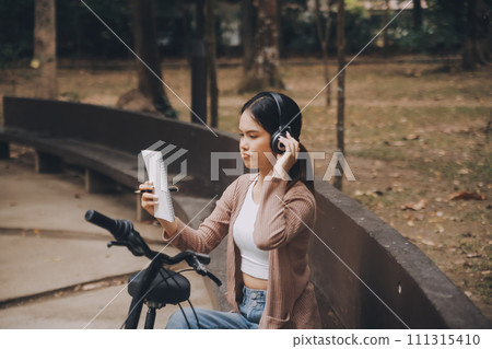 Happy young Asian woman while riding a bicycle in a city park. She smiled using the bicycle of transportation. Environmentally friendly concept. Happy young Asian woman while riding a bicycle in a city park. She smiled using the bicycle of transportation. Environmentally friendly concept. 111315410