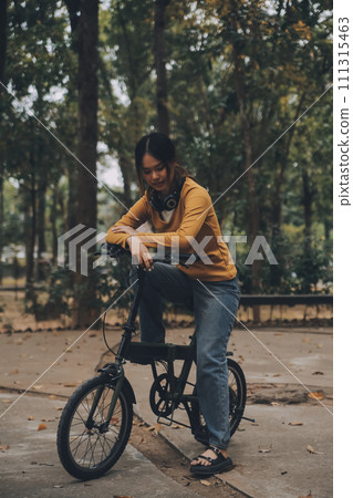 Happy young Asian woman while riding a bicycle in a city park. She smiled using the bicycle of transportation. Environmentally friendly concept. 111315463