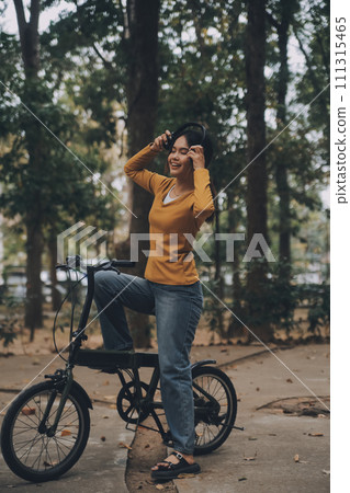 Happy young Asian woman while riding a bicycle in a city park. She smiled using the bicycle of transportation. Environmentally friendly concept. 111315465