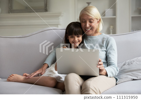 Happy grandmother and little granddaughter looking at laptop screen Happy grandmother and little granddaughter looking at laptop screen 111315950