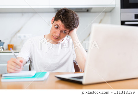 Upset man with laptop and utility bills in kitchen Upset man with laptop and utility bills in kitchen 111318159