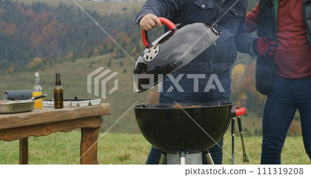Two men together cooking meat on BBQ grill on hill Two men together cooking meat on BBQ grill on hill 111319208