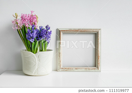 Wooden mock up photo frame and blooming hyacinth on a white table background Wooden mock up photo frame and blooming hyacinth on a white table background 111319977