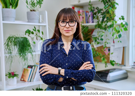 Portrait of confident smiling middle-aged woman with crossed arms at home 111320320